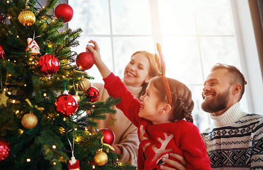 happy family mother, father and child daughter decorate Christmas tree at home