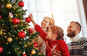 happy family mother, father and child daughter decorate Christmas tree