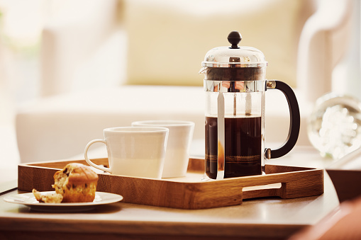 Cup of fresh coffee and a french press on the tray with cupcake