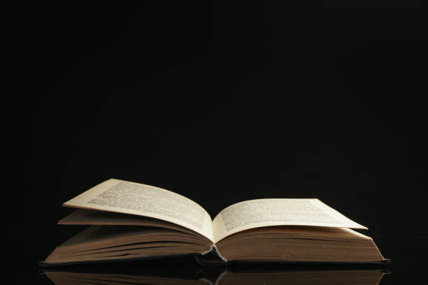 istock One open old book on a glass table. Beautiful dark background.. 1185862760