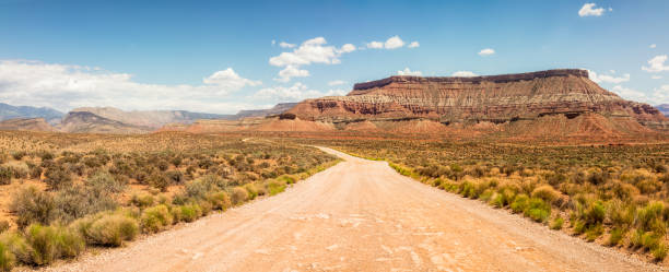 Wide open American wilderness Rock formations surrounding a winding dirt road in southern Utah, USA. panoramic country road single lane road sky stock pictures, royalty-free photos & images