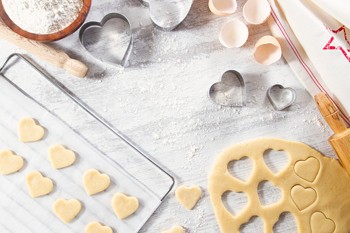 Making of heart shaped cookies with pastry dough and cookie cutter on white kitchen counter