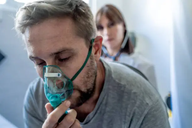 Young sick man patient with Oxygen Mask while female doctor listens his chest with stethoscope in hospital emergency room. In Smoking, respiratory diseases and Health care anti tobacco advertising campaign.
