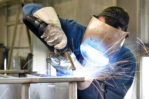Male worker welding steel, sparks from light, protective masks and gloves increase safety