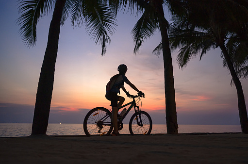 silhouette of woman riding bicycle along the sea beach at sunset