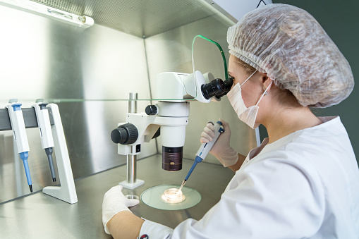 An embryologist works with human cells under a microscope.