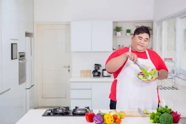 Picture of overweight man mixing fresh vegetables in a bowl while standing in the kitchen