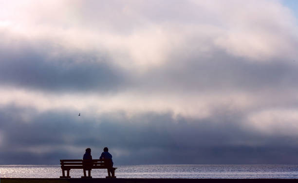 istock Two people sitting on a street bench and watching the dramatic sunset 1185881033