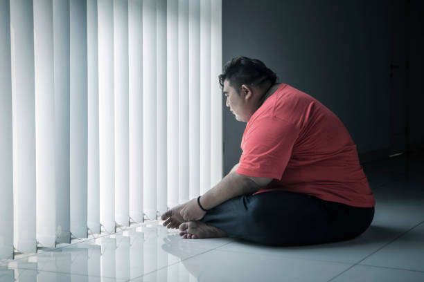 istock Pensive fat man sitting near the window 1185882536