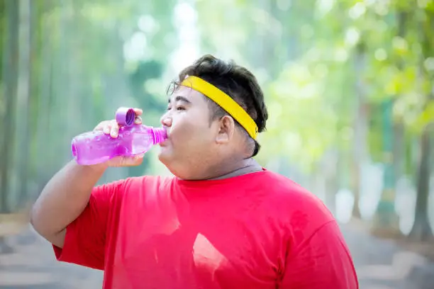 Picture of fat man looks tired while drinking a bottle of water after exercising in the park