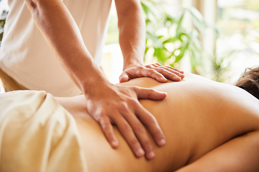 Closeup of a male massage therapist's hands working on the back of a woman on a table in his clinic