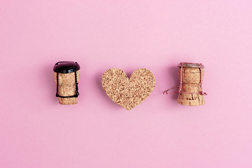Girl and boy characters from champagne corks and muselets with heart on pink colored background. Concept for Valentines Day or wedding on topic of relations between man and woman. Flat lay.