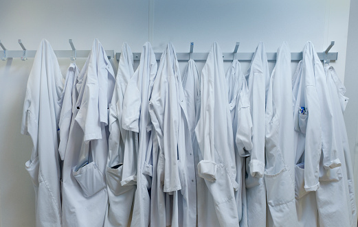 Lab coats hanging from hooks at laboratory. White workwear are against wall. It is in place of research.