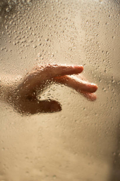 istock young womans hand behind a glass with water drops 1185886417