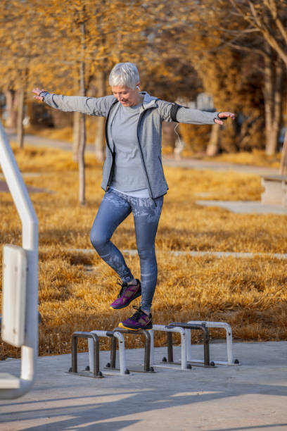 Beautiful mature senior woman in sportswear have fitness training in public park. She is exercise balance with outstretched arms and listening music.
