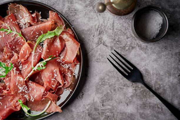 smaczna apetyczny klasyczny włoski bresaola z sałatką z rakiety i parmezanem na czarnym talerzu na czarnym tle. wyświetl formularz powyżej - beef carpaccio zdjęcia i obrazy z banku zdjęć