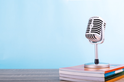 Education teaching concept : Retro microphone with many book put on wooden table isolated on blue background.