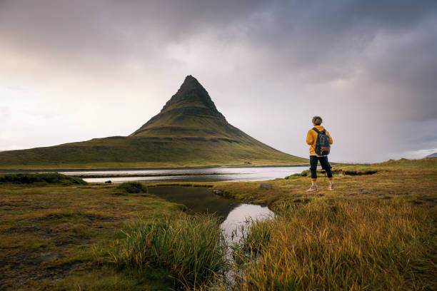 joven excursionista con una mochila mira a la montaña kirkjufell en islandia - snaefellsnes fotografías e imágenes de stock