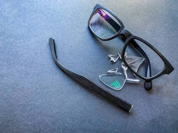 Photo of plastic glasses with a broken lens and a torn earhook on a dark background.