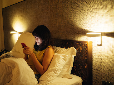 Young asian woman using smartphone for sharing social media lying in bed at home at night. Bangkok, Thailand.