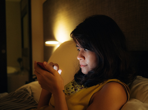 Young asian woman using smartphone for sharing social media lying in bed at home at night. Bangkok, Thailand.