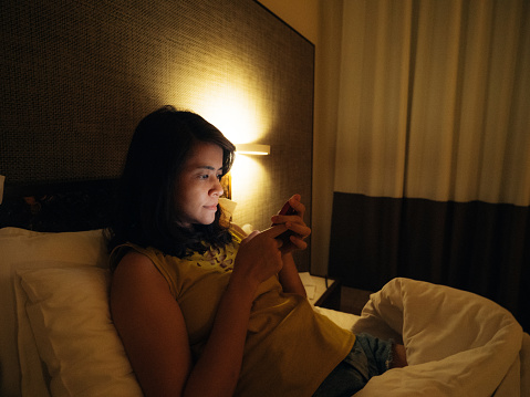 Asian woman surfing the net on smart phone in the room at night. Bangkok, Thailand.