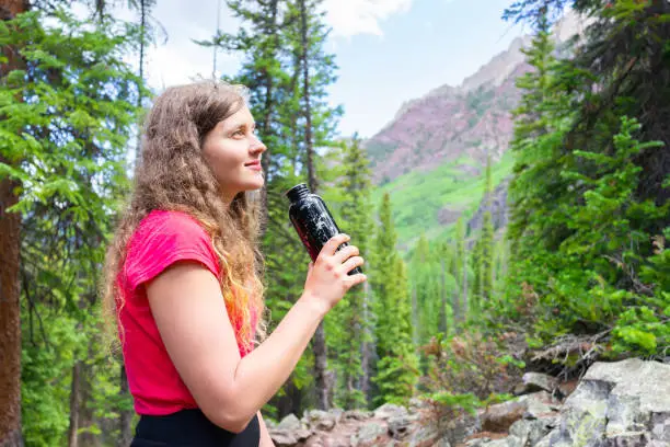 Young girl happy thirsty woman stopping for drinking water on hike on Snowmass Lake Trail in Aspen, Colorado in 2019 summer
