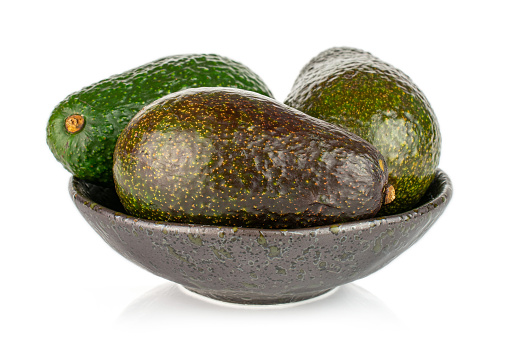 Group of three whole fresh green avocado in dark ceramic bowl isolated on white background