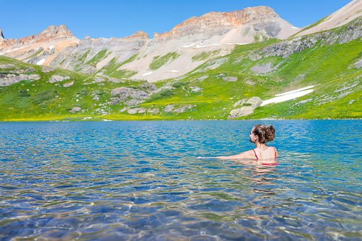 Young woman girl swimming cold colorful water of Ice Lake on famous trail in Silverton, Colorado in San Juan Mountains in summer
