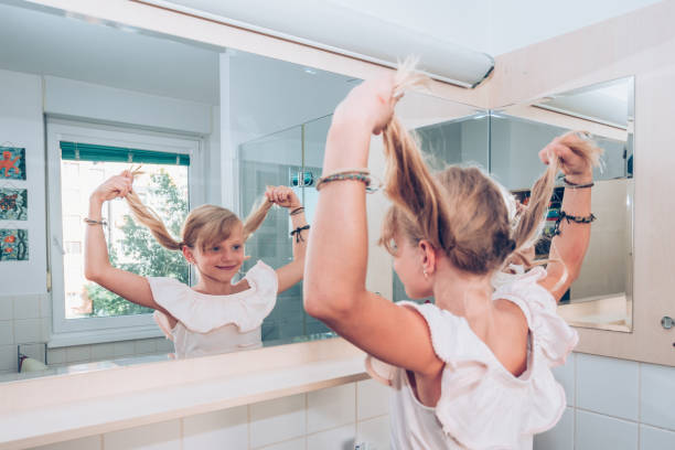 istock lovely blond child in the bathroom having fun with two long blond tails while looking into the mirror 1185916689