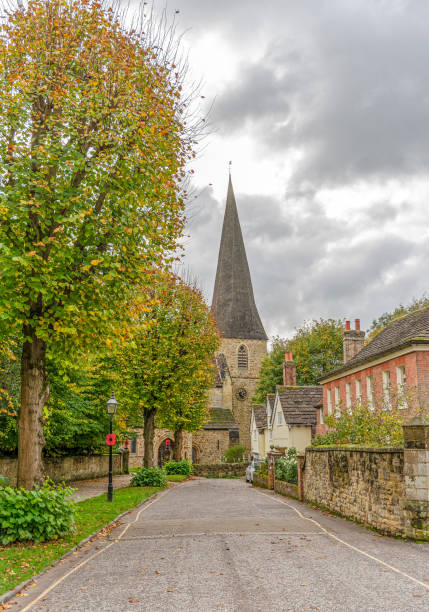 A wide view of St Georges Church in Crowhurst, Surrey., with a field and treeline in the foreground and an overcast, moody sky.