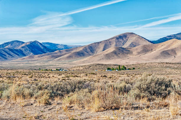 This country view in the Reno Nevada area shows the beautiful hills in the background under a cloudy sky with farms in the meadow.