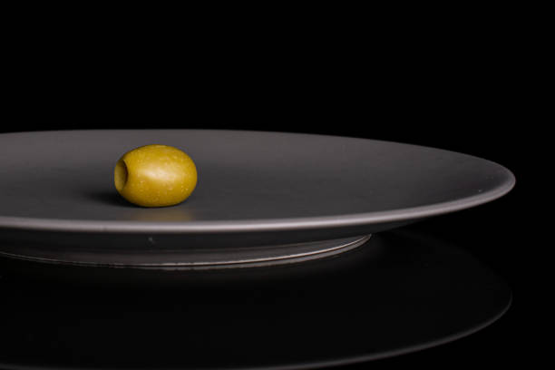 One whole pitted green olive on gray ceramic plate isolated on black glass