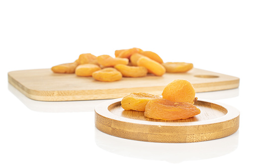 Lot of whole dried orange apricot on bamboo cutting board on round bamboo coaster isolated on white background