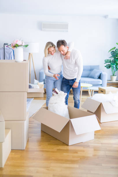 istock Young beautiful couple with dog hugging at new home around cardboard boxes 1185923607