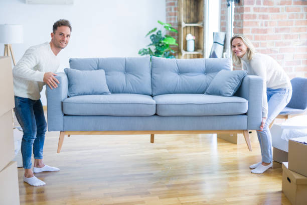 istock Young beautiful couple moving sofa at new home around cardboard boxes 1185924349
