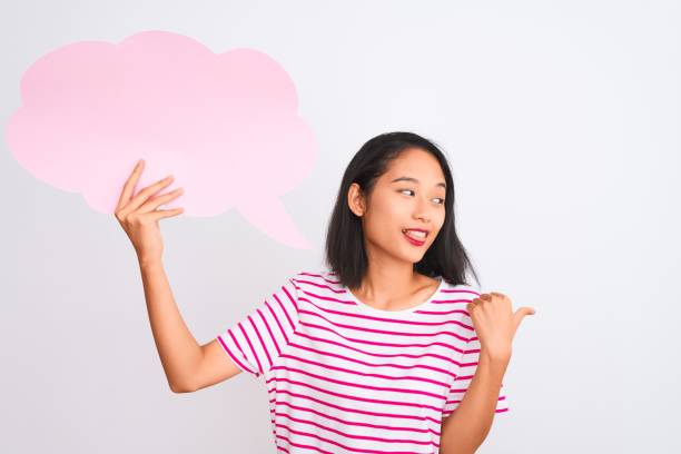 istock Young chinese woman holding cloud speech bubble standing over isolated white background pointing and showing with thumb up to the side with happy face smiling 1185924747