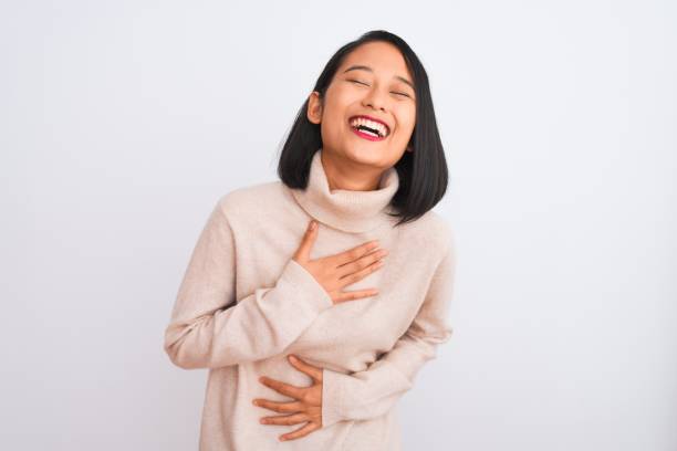 Young chinese woman wearing turtleneck sweater standing over isolated white background smiling and laughing hard out loud because funny crazy joke with hands on body. Young chinese woman wearing turtleneck sweater standing over isolated white background smiling and laughing hard out loud because funny crazy joke with hands on body. people laughing hard stock pictures, royalty-free photos & images
