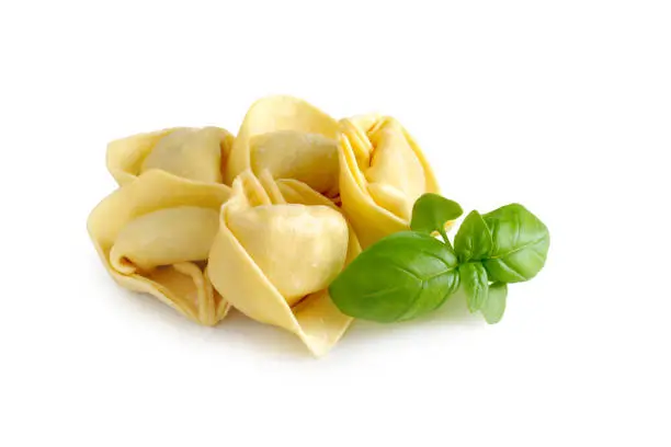 Raw fresh tortellini pasta with basil leaves isolated on white background