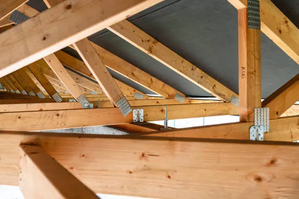Photo of Roof trusses covered with a membrane on a detached house under construction, view from the inside, visible roof elements and truss plates.