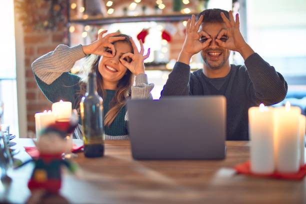 istock Young beautiful couple sitting using laptop around christmas decoration at home doing ok gesture like binoculars sticking tongue out, eyes looking through fingers. Crazy expression. 1185931411
