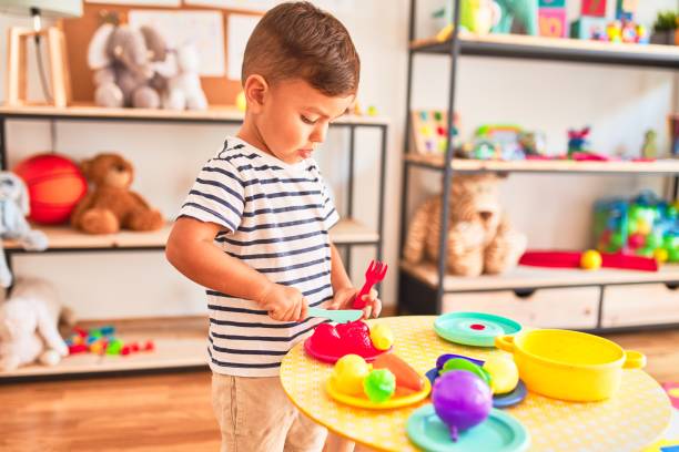 beautiful toddler boy playing meals with plastic plates, fruits and vegetables at kindergarten - preschooler child playing latin american and hispanic ethnicity imagens e fotografias de stock