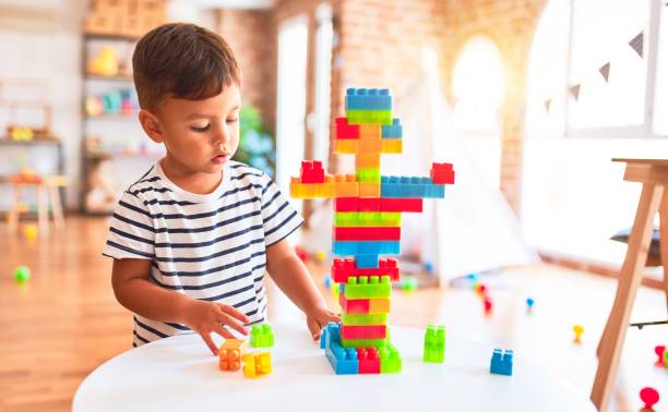 schöne kleinkind junge spielen mit bauklötzen im kindergarten - bauklotz stock-fotos und bilder