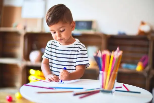 Beautiful toddler boy drawing cute draw using colored pencils at kindergarten