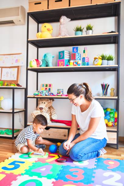 istock Beautiful teacher and toddler boy drawing draw using digital board at kindergarten 1185932134