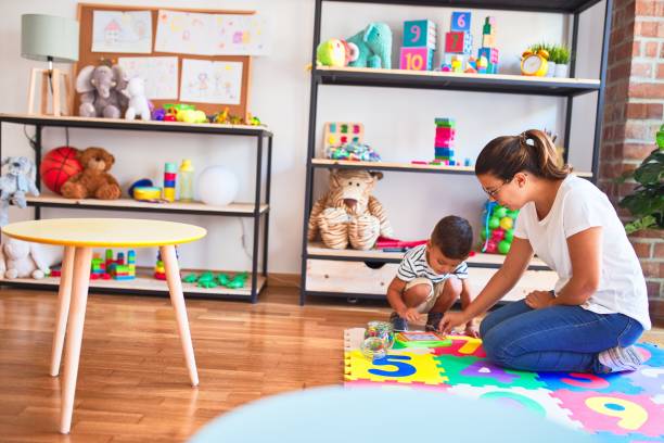 istock Beautiful teacher and toddler boy drawing draw using digital board at kindergarten 1185932154