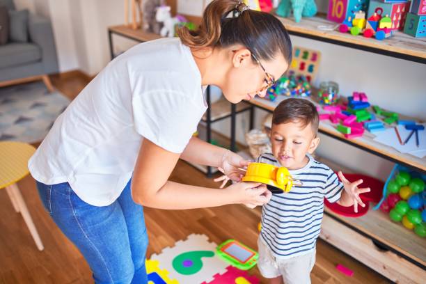 schöne lehrerin und kleinkind mit wecker im kindergarten - child playroom parent indoors stock-fotos und bilder