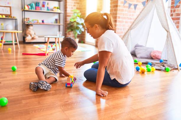 istock Beautiful teacher and toddler boy playing with train at kindergarten 1185932449