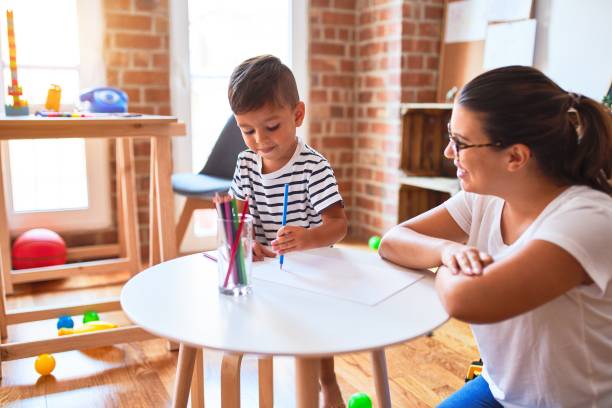 schöne lehrer und kleinkind junge zeichnung zeichnung mit buntstiften im kindergarten - child playroom parent indoors stock-fotos und bilder