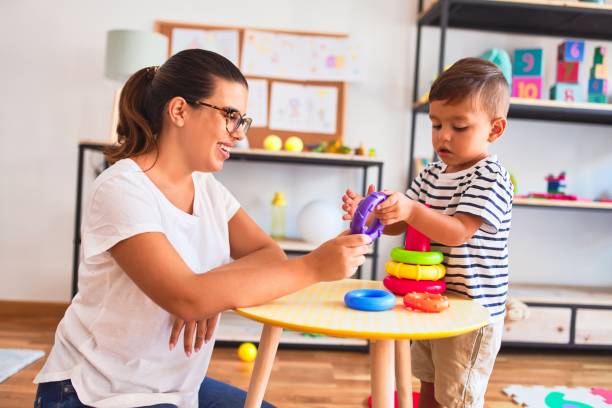 schöne lehrer und kleinkind junge gebäude pyramide mit reifen bolcks im kindergarten - child playroom parent indoors stock-fotos und bilder